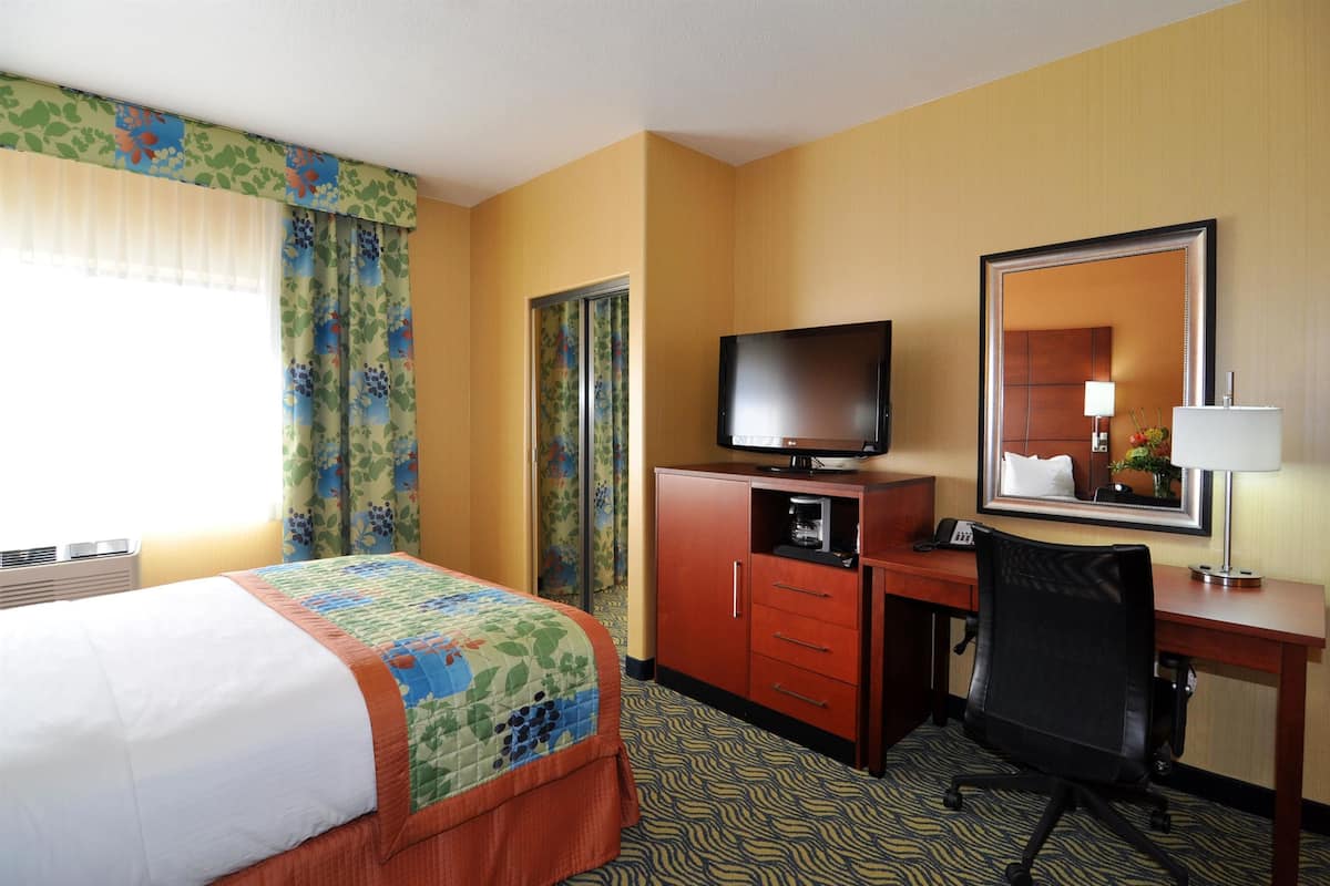 A hotel room with a bed, a desk with a computer, a television, and a mirror.