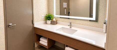 Un baño moderno con un espejo grande, un lavamanos, un perchero para toallas y una planta en maceta.