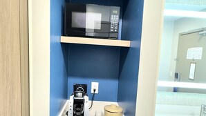 Una kitchenette compacta con microondas, cafetera y refrigerador.