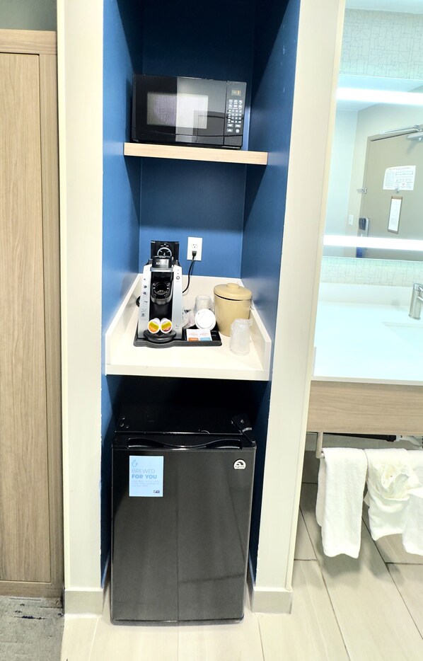 Una kitchenette compacta con microondas, cafetera y refrigerador.