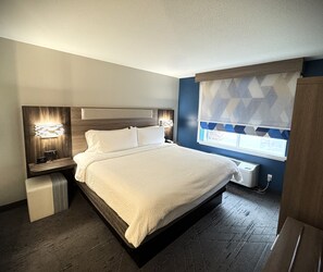 Een moderne hotelkamer met een groot bed, nachtkastjes met lampen, een raam met patroongordijnen en een ingebouwde airconditioning.
