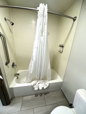 Una ducha con cortina blanca, barra de apoyo y cabezal de ducha manual.