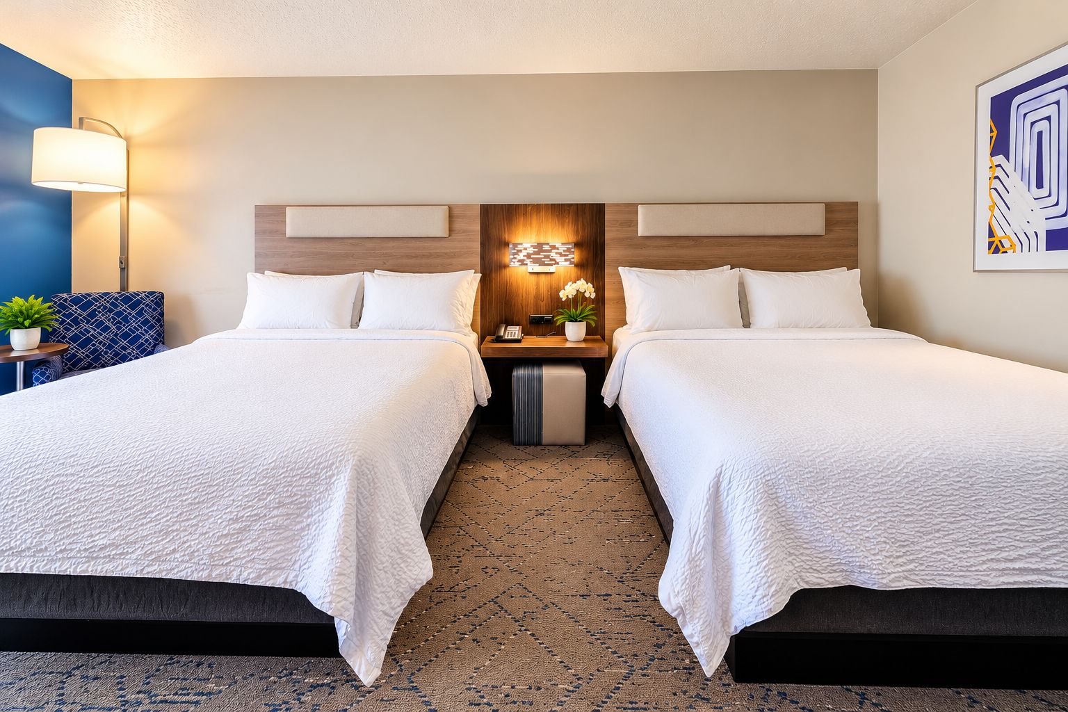 A hotel room with two beds, a nightstand, a lamp, and a wall-mounted artwork.