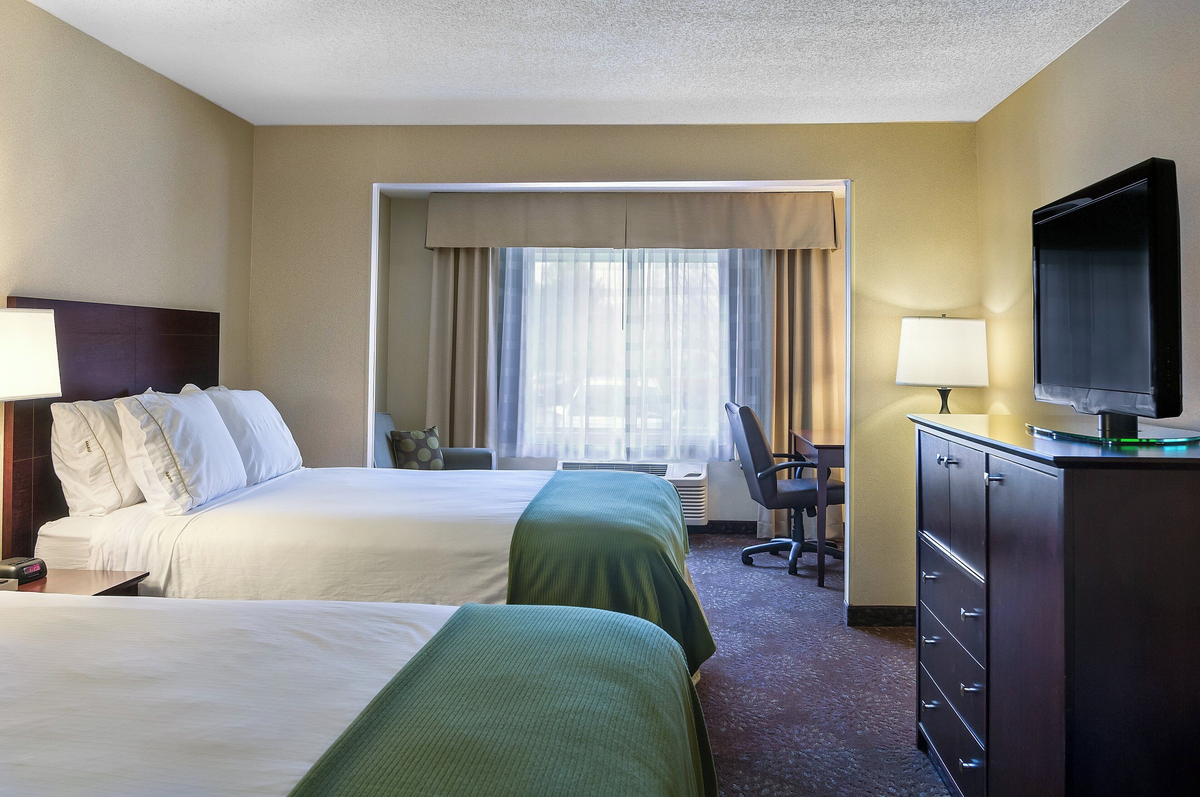 A hotel room with two beds, a television, a desk, and a chair.