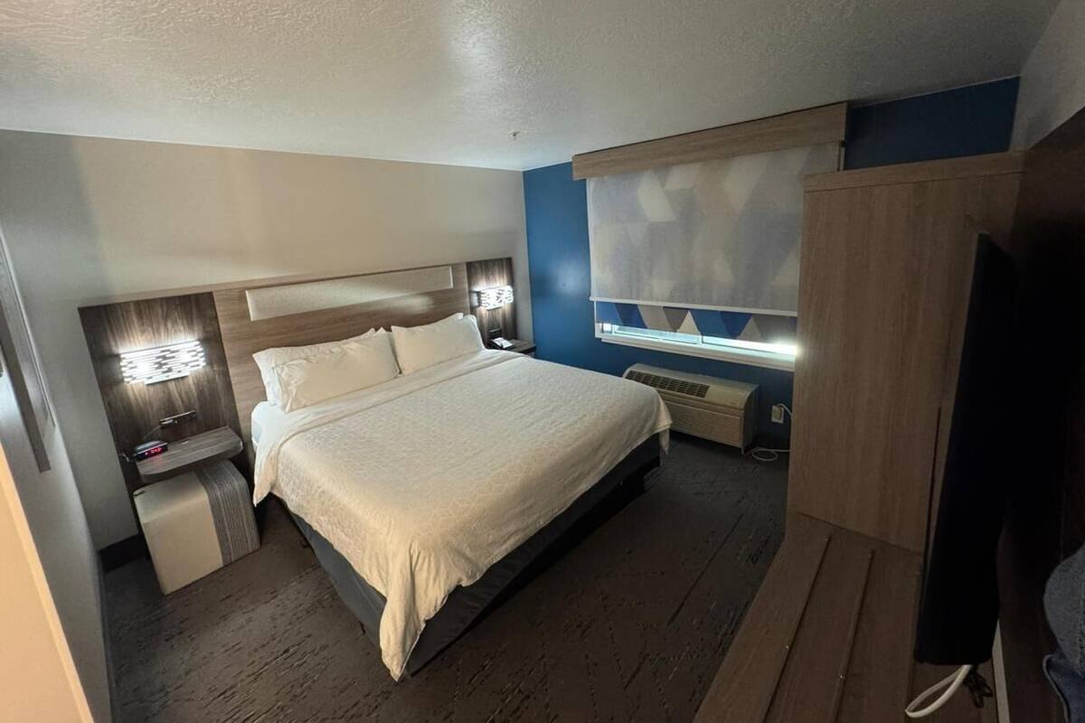 Un dormitorio con cama, mesitas de noche, un armario y una ventana con persianas.