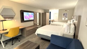 Habitación de hotel con cama, sofá, escritorio con silla, televisor y espejo en la pared.