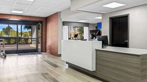 A modern reception area with a wooden reception desk, a computer, and a view through the glass doors. - Clarion Pointe Franklin - Nashville Area (Franklin)