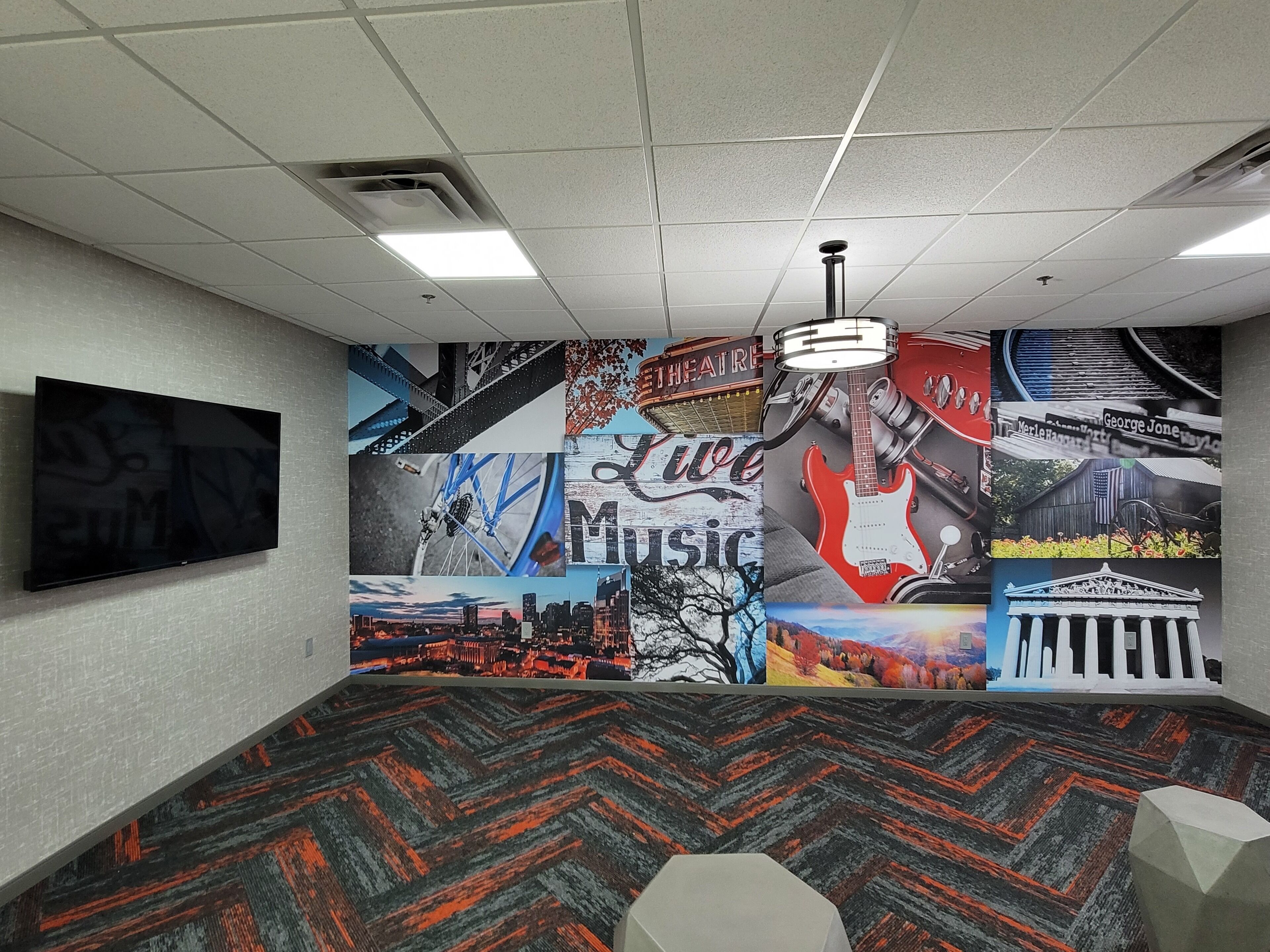 A conference room with a large mural on the wall depicting various music and city scenes, a flat-screen TV mounted on the wall, and a patterned carpet.