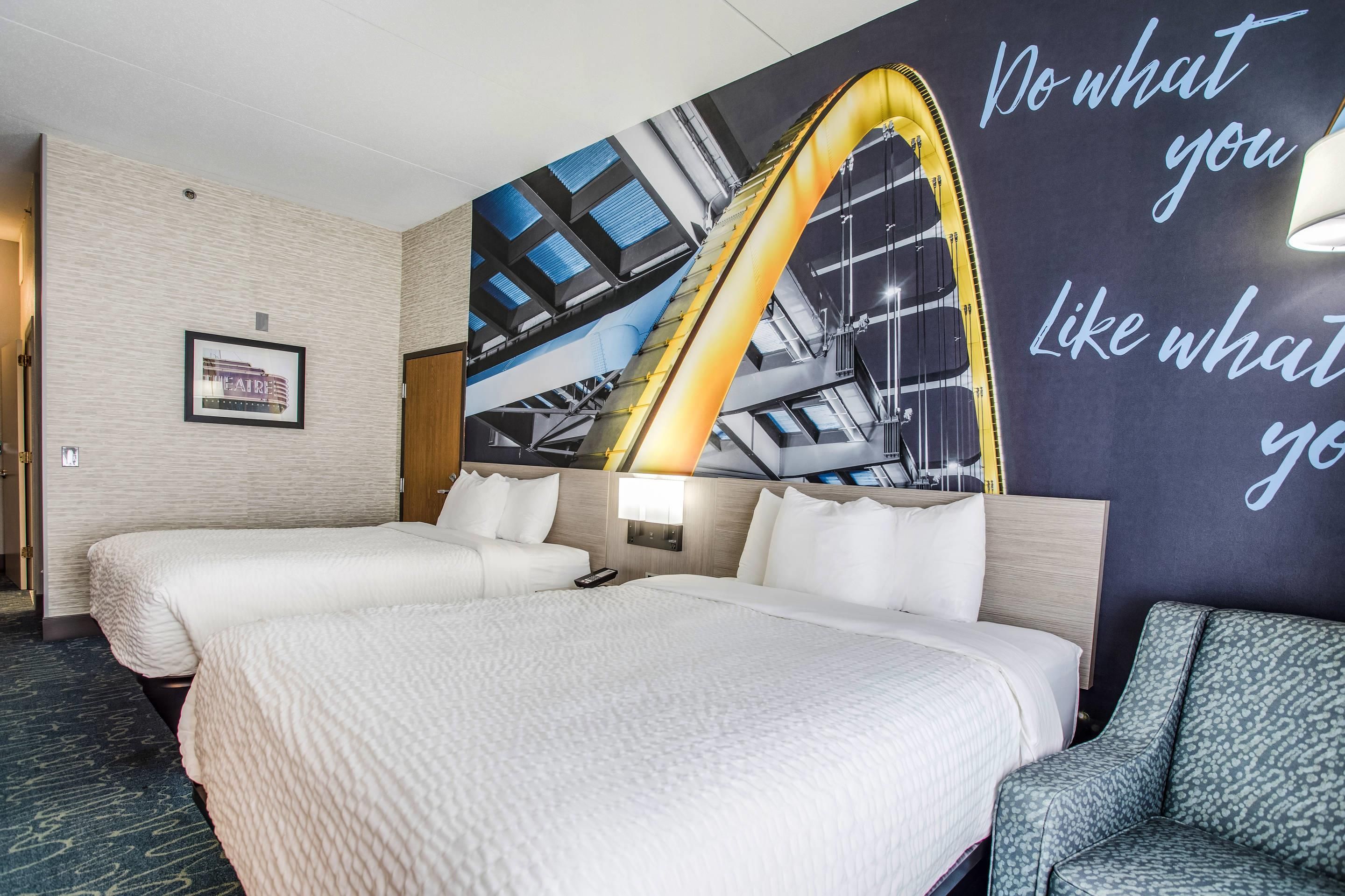 Habitació d'hotel amb dos llits, un mural gran a la paret i una frase motivacional.