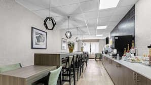 A modern kitchen with a long counter, multiple chairs, hanging pendant lights, and a refrigerator. - Clarion Pointe Franklin - Nashville Area (Franklin)