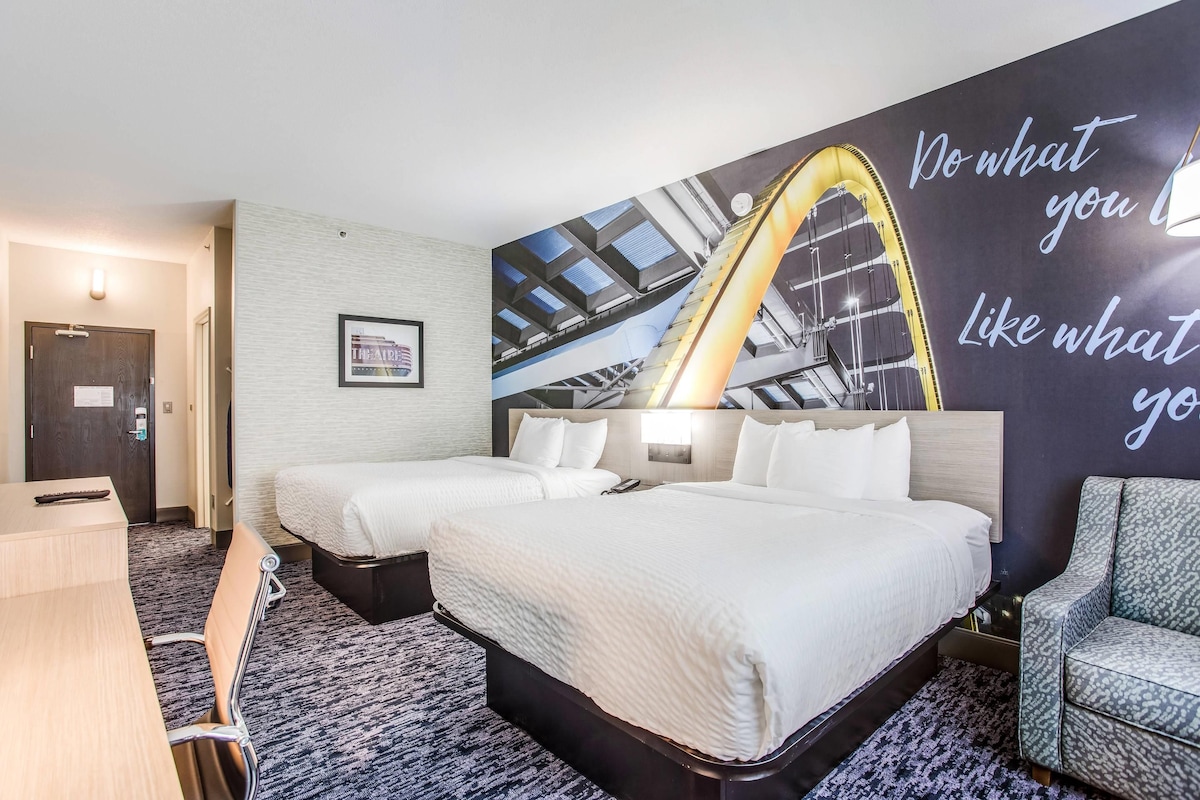 A hotel room with two beds, a desk, and a large wall mural.
