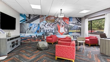 A hotel room with a cityscape mural, red patterned sofas, a desk, and a television.
