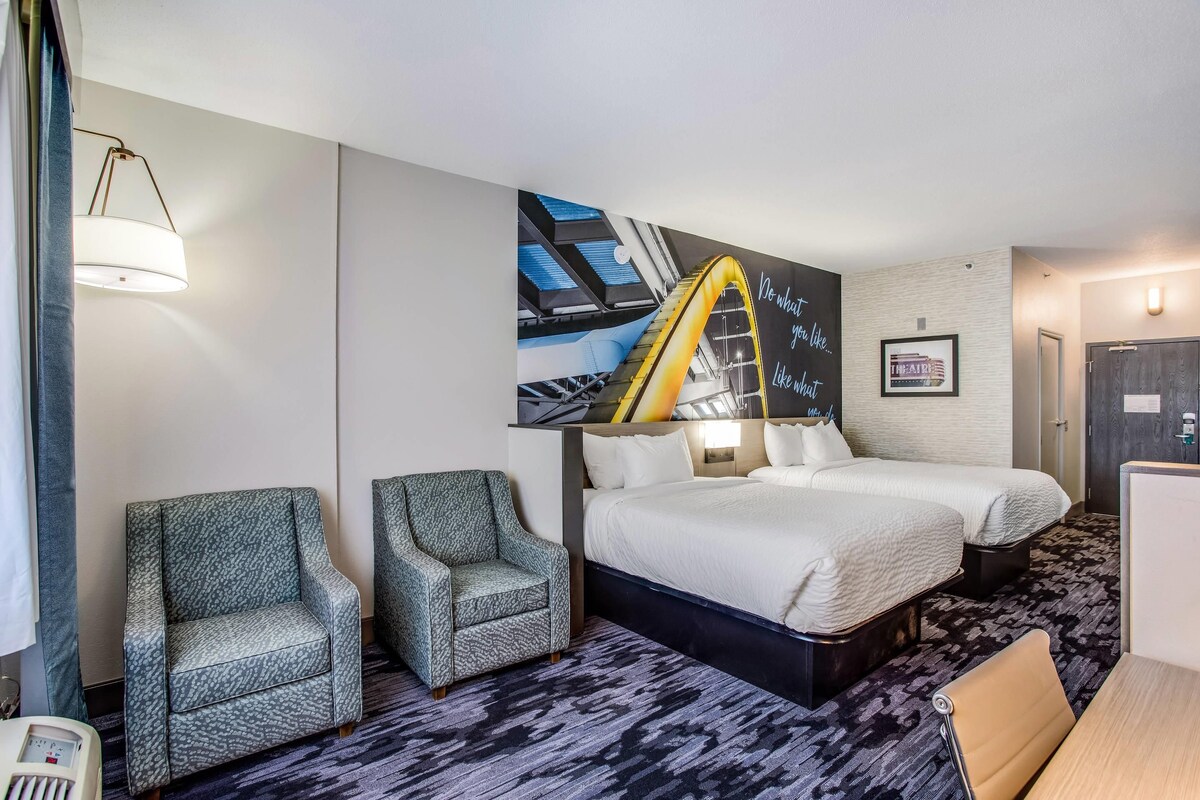 A hotel room with a bed, two armchairs, a desk, and a large wall mural.