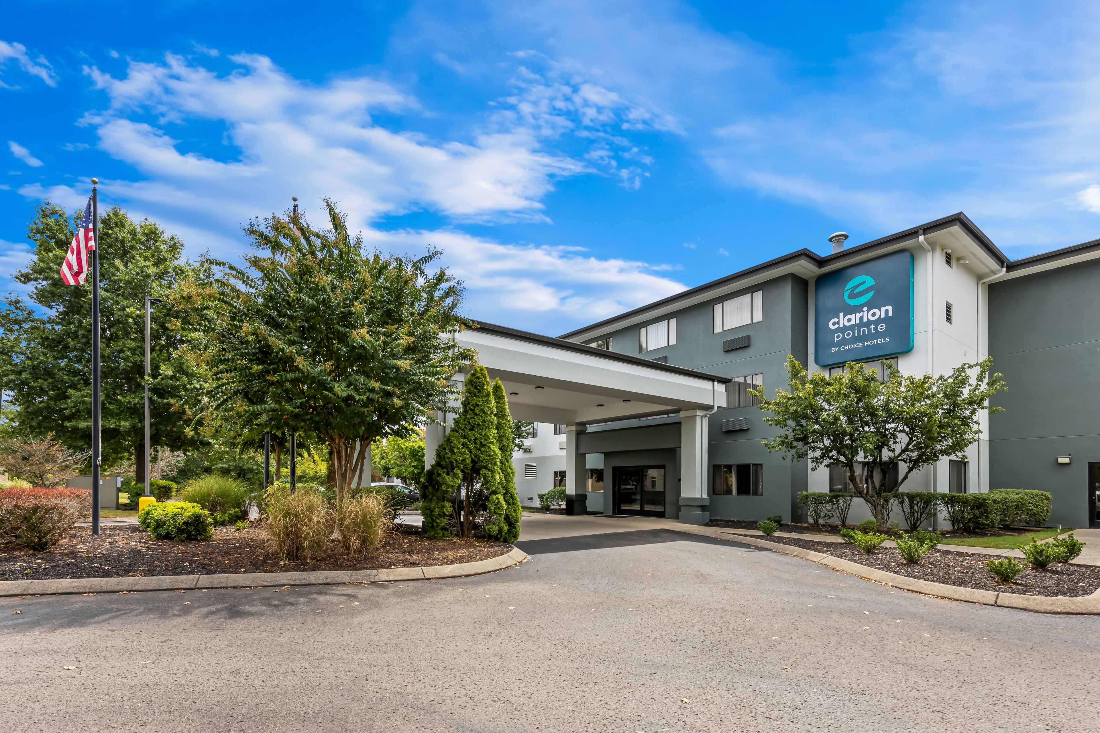 A hotel entrance with a covered walkway, American flag, and a sign for Clarion Pointe by Choice Hotels.