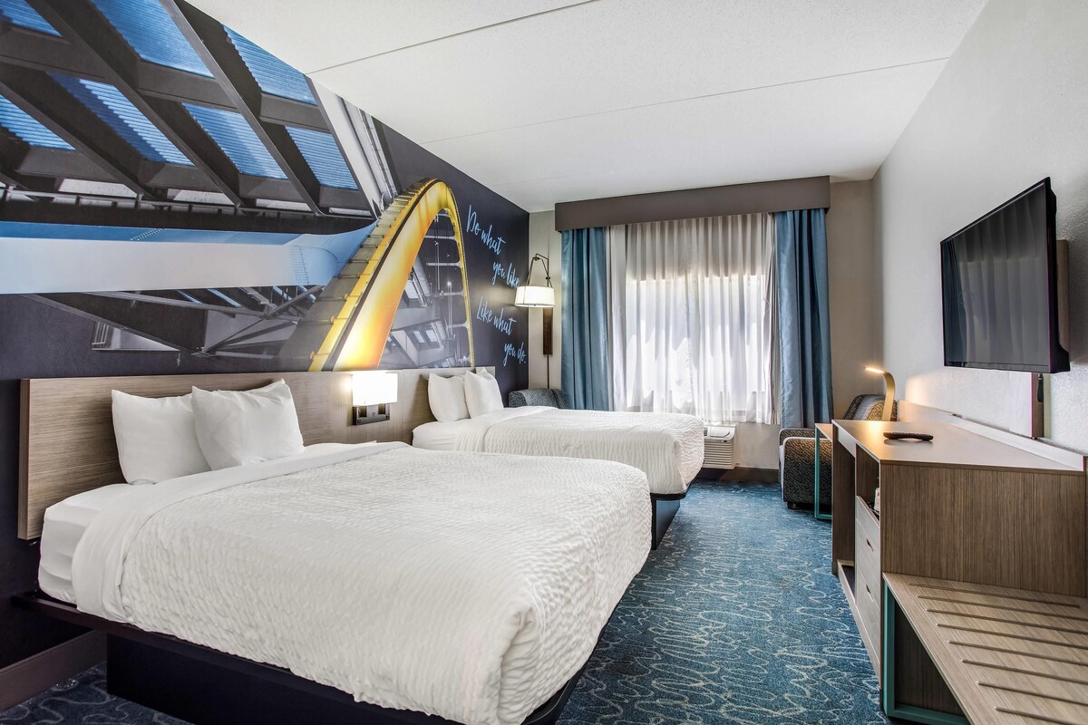 A hotel room with two beds, a desk, a TV, and a mural of a roller coaster.