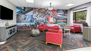 A hotel room with a cityscape mural, red patterned sofas, a flat-screen TV, and a desk with a chair. - Clarion Pointe Franklin - Nashville Area (Franklin)