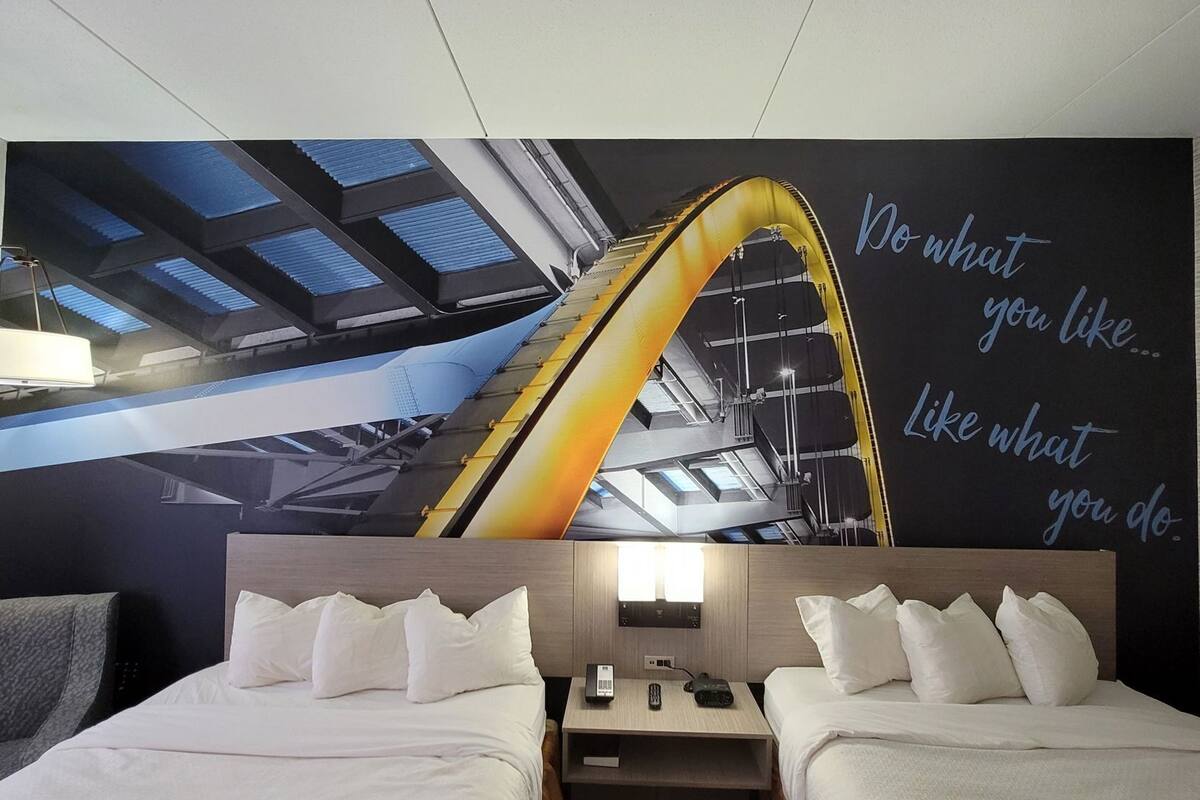 A hotel room with two beds, a large wall mural of a roller coaster, and a motivational quote.