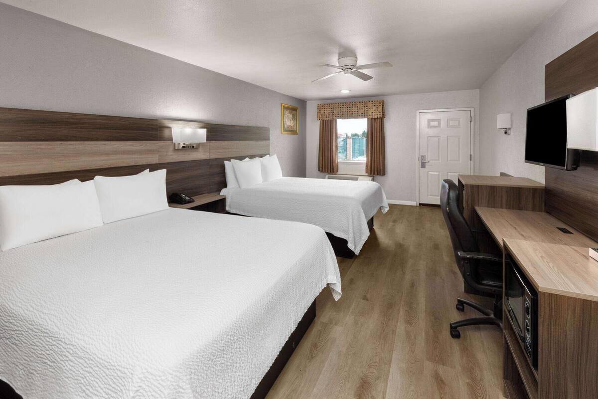 A hotel room with two beds, a desk with a chair, a television, and a ceiling fan.
