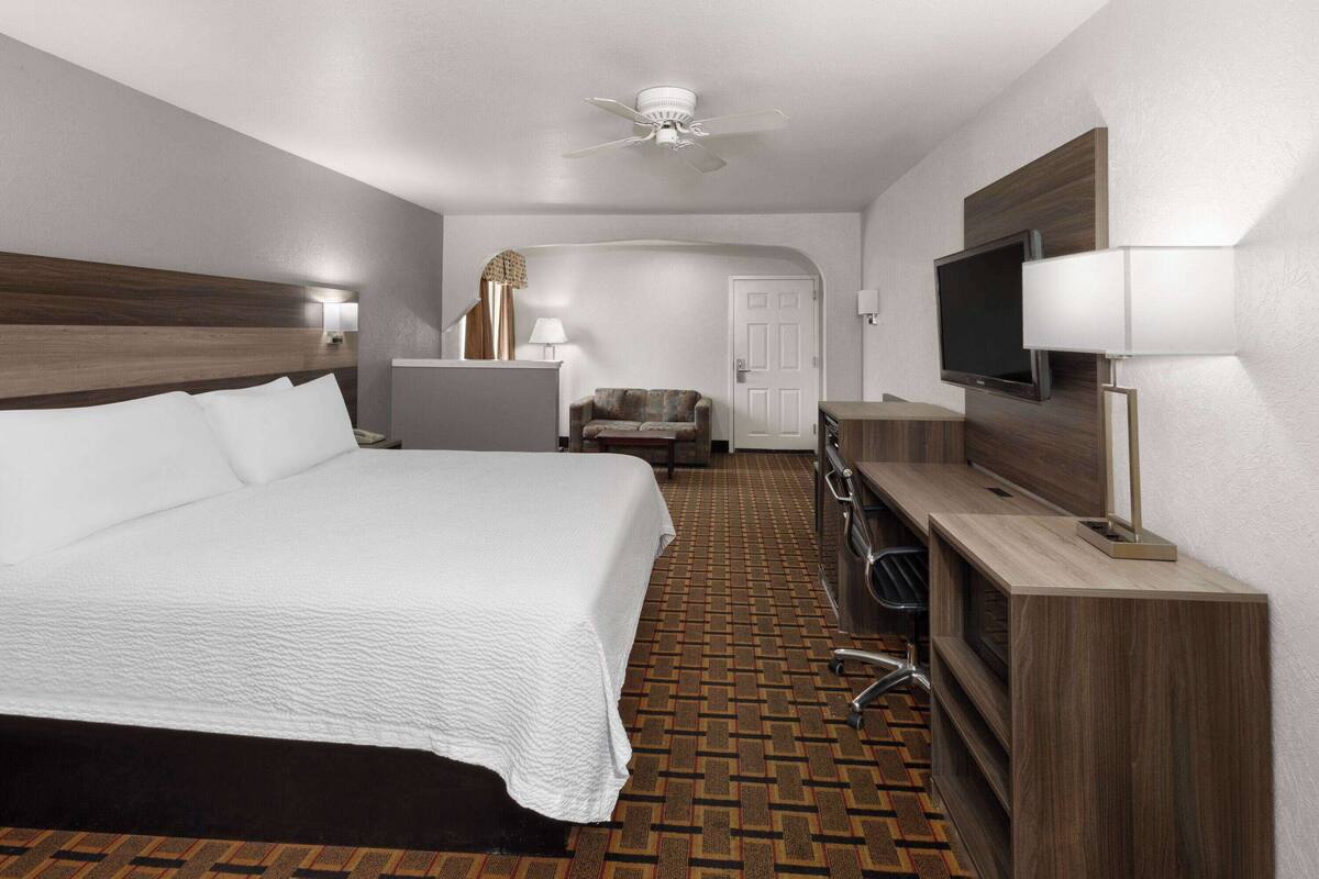 A hotel room with a large bed, a desk with a flat-screen TV, a chair, and a ceiling fan.