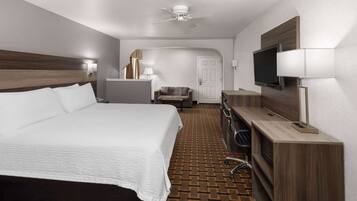 A hotel room with a large bed, a desk with a flat-screen TV, a chair, and a ceiling fan.