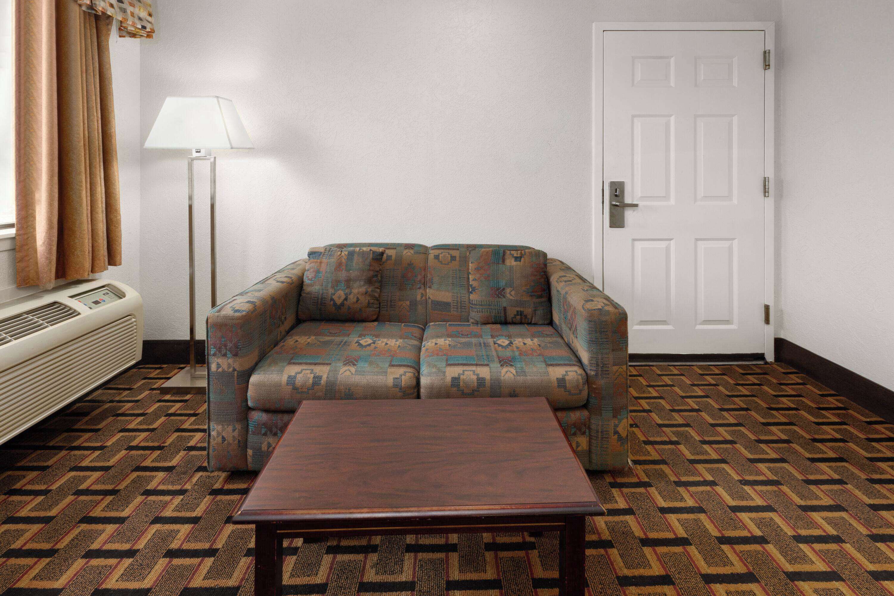 A room with a patterned sofa, a small wooden table, a floor lamp, and a white door.