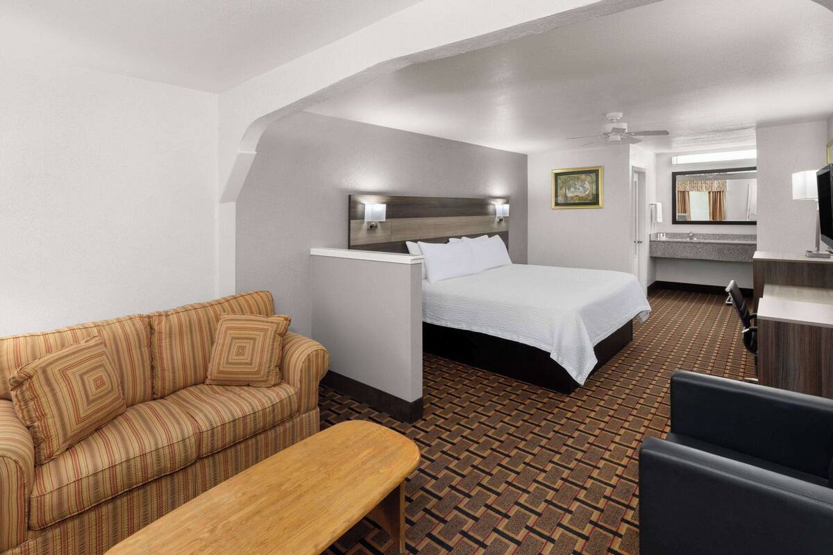 A hotel room with a bed, a sofa, a small table, a desk, and a mirror.