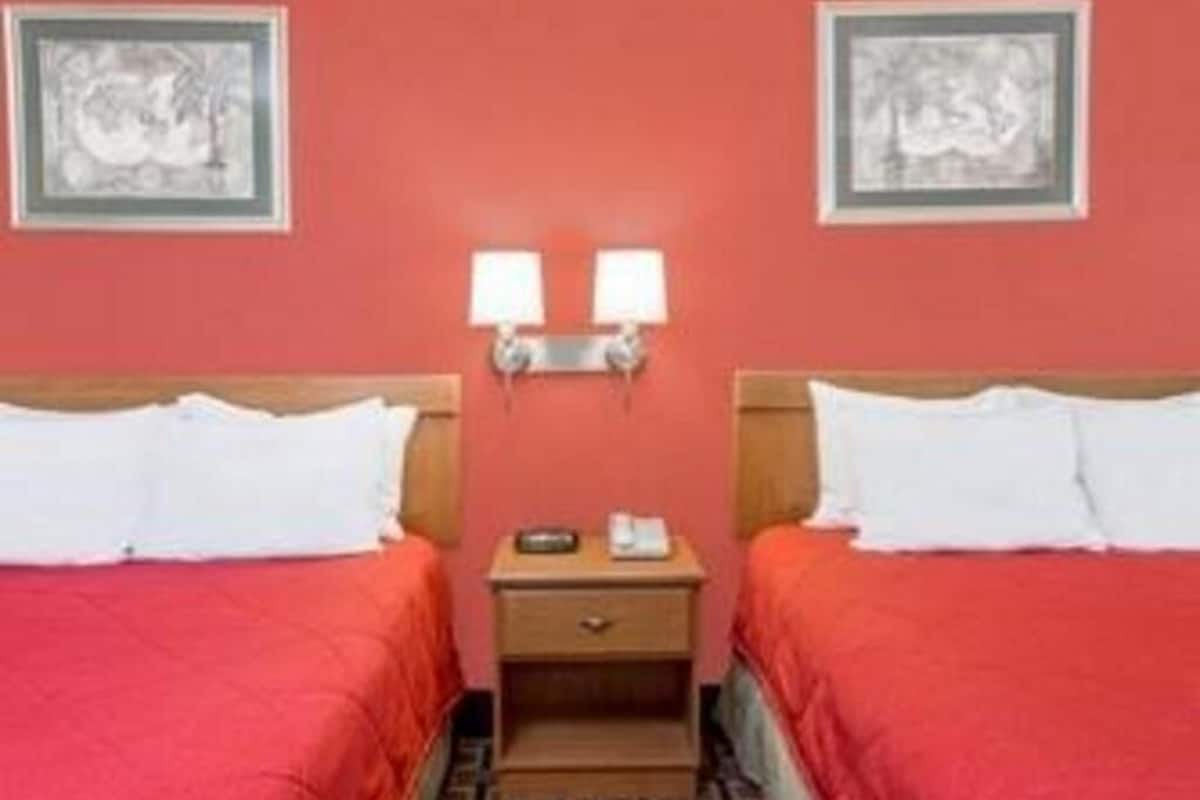 A hotel room with two beds, a nightstand, two wall-mounted lamps, and two framed pictures on the walls.