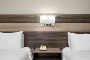 A hotel room with two beds, a bedside table with a telephone, and a wall-mounted light fixture. - Ramada Limited San Angelo (San Angelo)
