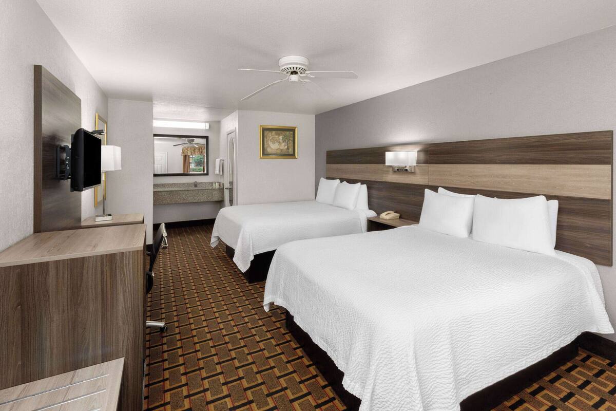 A hotel room with two beds, a TV, a desk, and a bathroom visible through an open door.