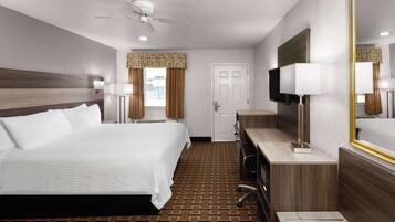 A hotel room with a large bed, a desk, a TV, and a ceiling fan.