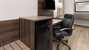 Ein Hotelzimmer mit einem Holztisch, einem schwarzen Bürostuhl, einem an der Wand befestigten Fernseher, einer Lampe und einem Spiegel über einem Spiegel.