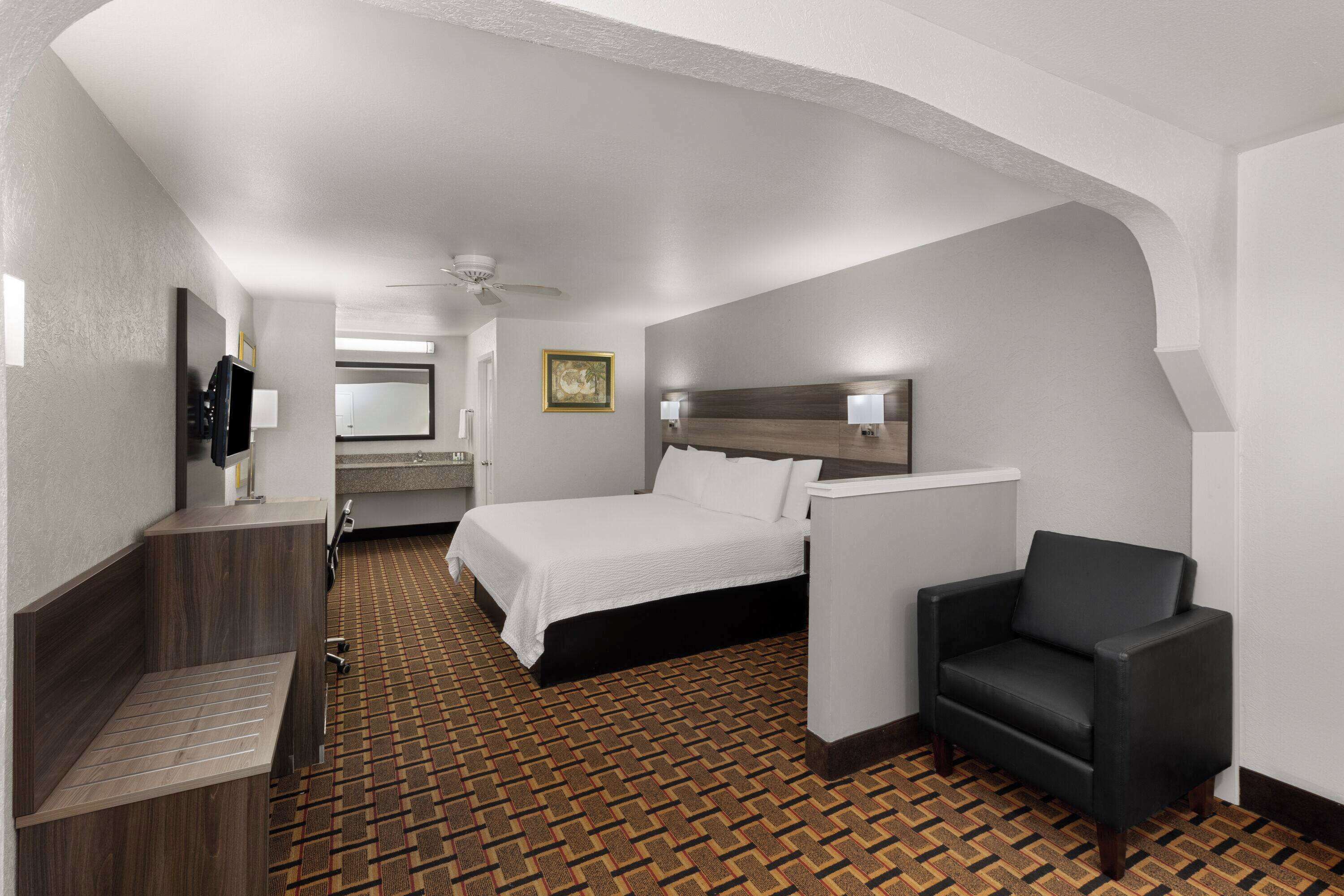 Quarto de hotel com cama, cadeira, escrivaninha, televisão e banheiro.