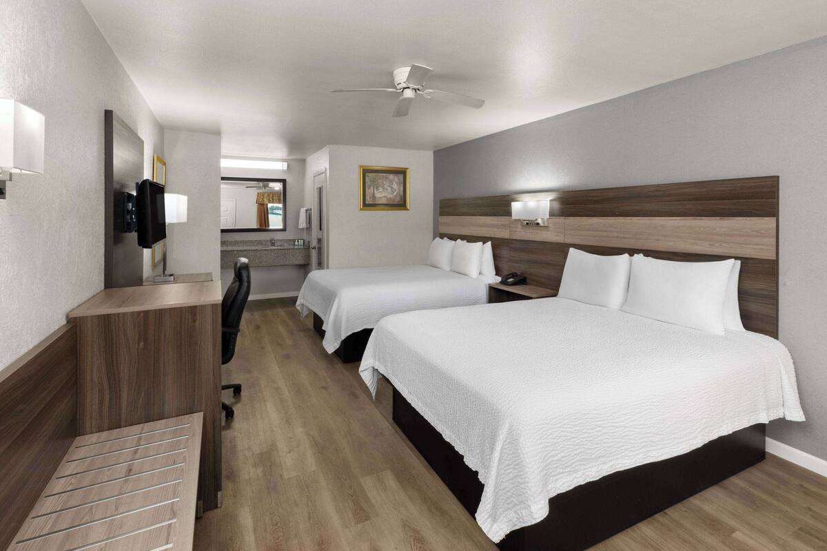 A hotel room with two beds, a desk, a chair, a television, and a ceiling fan.