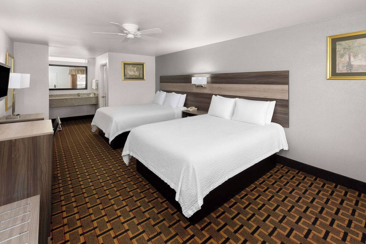 A hotel room with two beds, a desk, a television, and a ceiling fan.