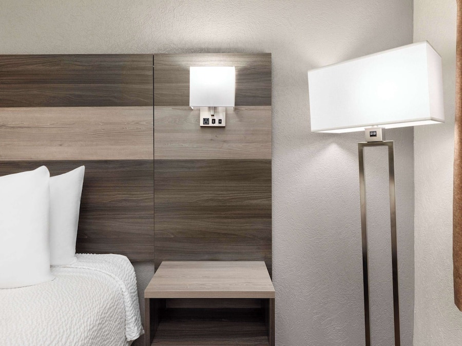 Ett hotellrum med en säng, ett sängbord, en väggmonterad lampa och ett litet bord.