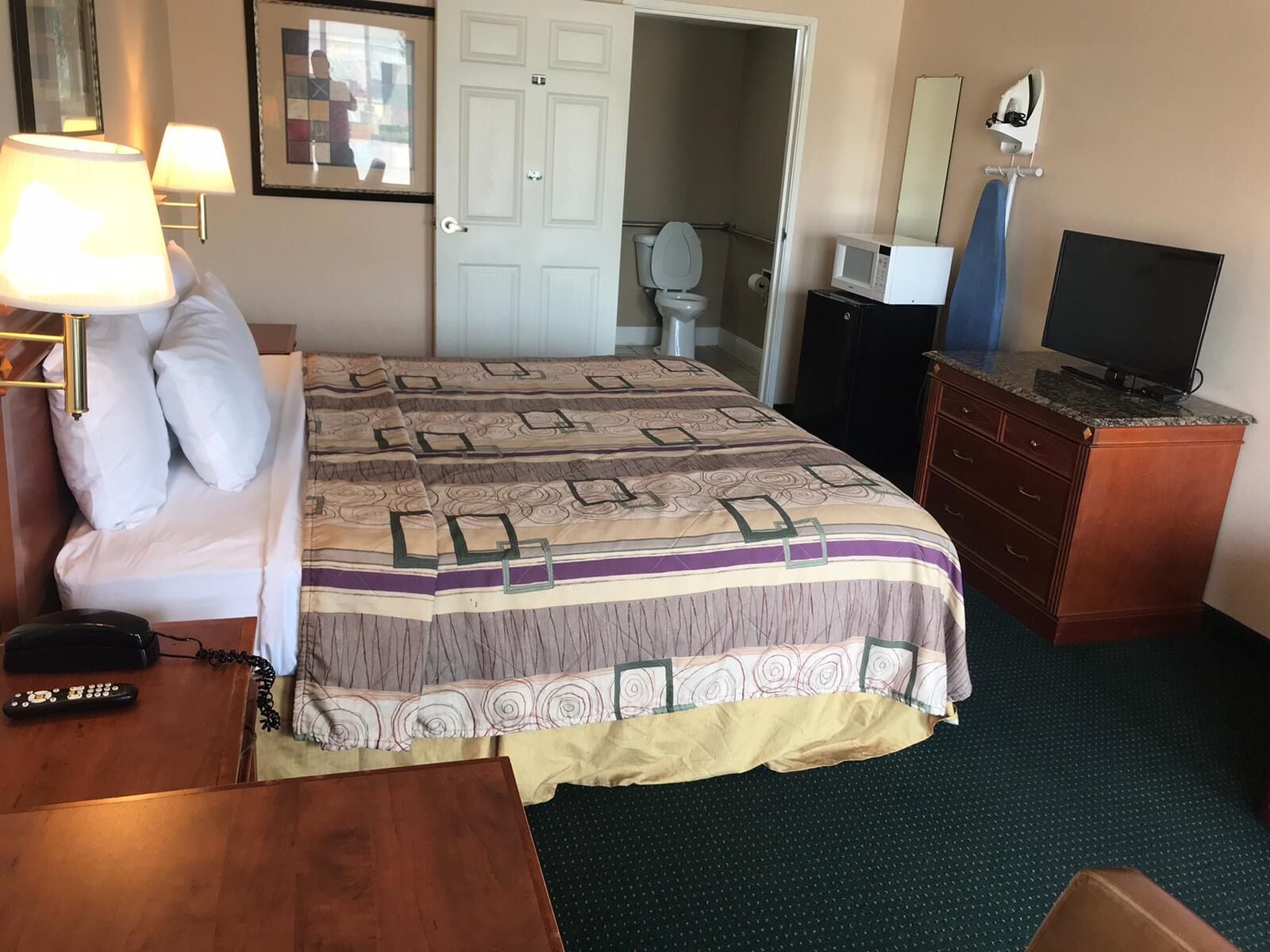 Habitación de hotel con una cama, lámparas de noche, televisión, cómoda, microondas y una puerta que da a un baño.