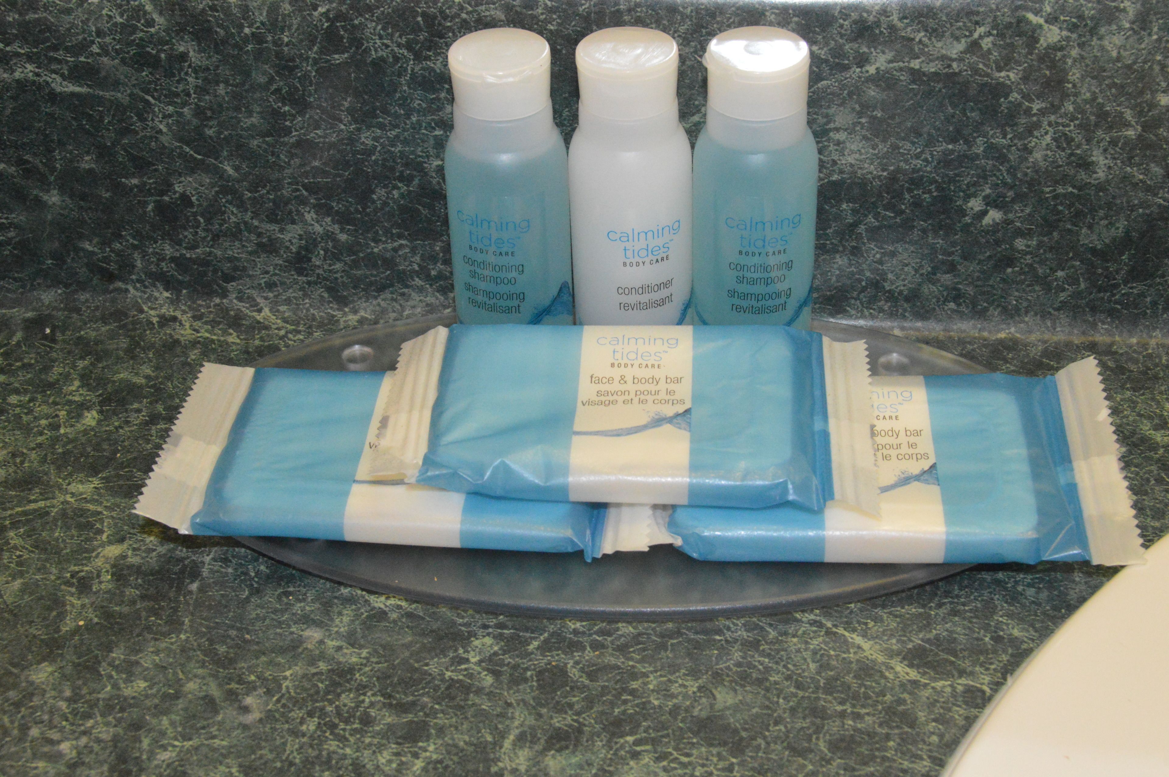 Una encimera de baño con tres botellas de productos de cuidado corporal y tres pastillas exfoliantes para cuerpo y rostro.