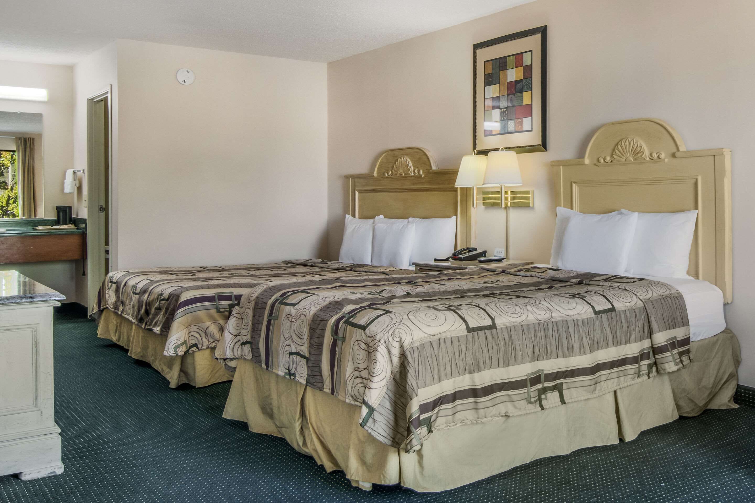 Habitación de hotel con dos camas, un escritorio y una lámpara.