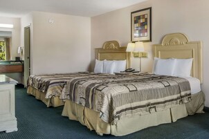 Habitación de hotel con dos camas, un escritorio y una lámpara.