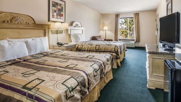 Une chambre d’hôtel avec deux lits, une télévision, un bureau et une fenêtre avec des rideaux.