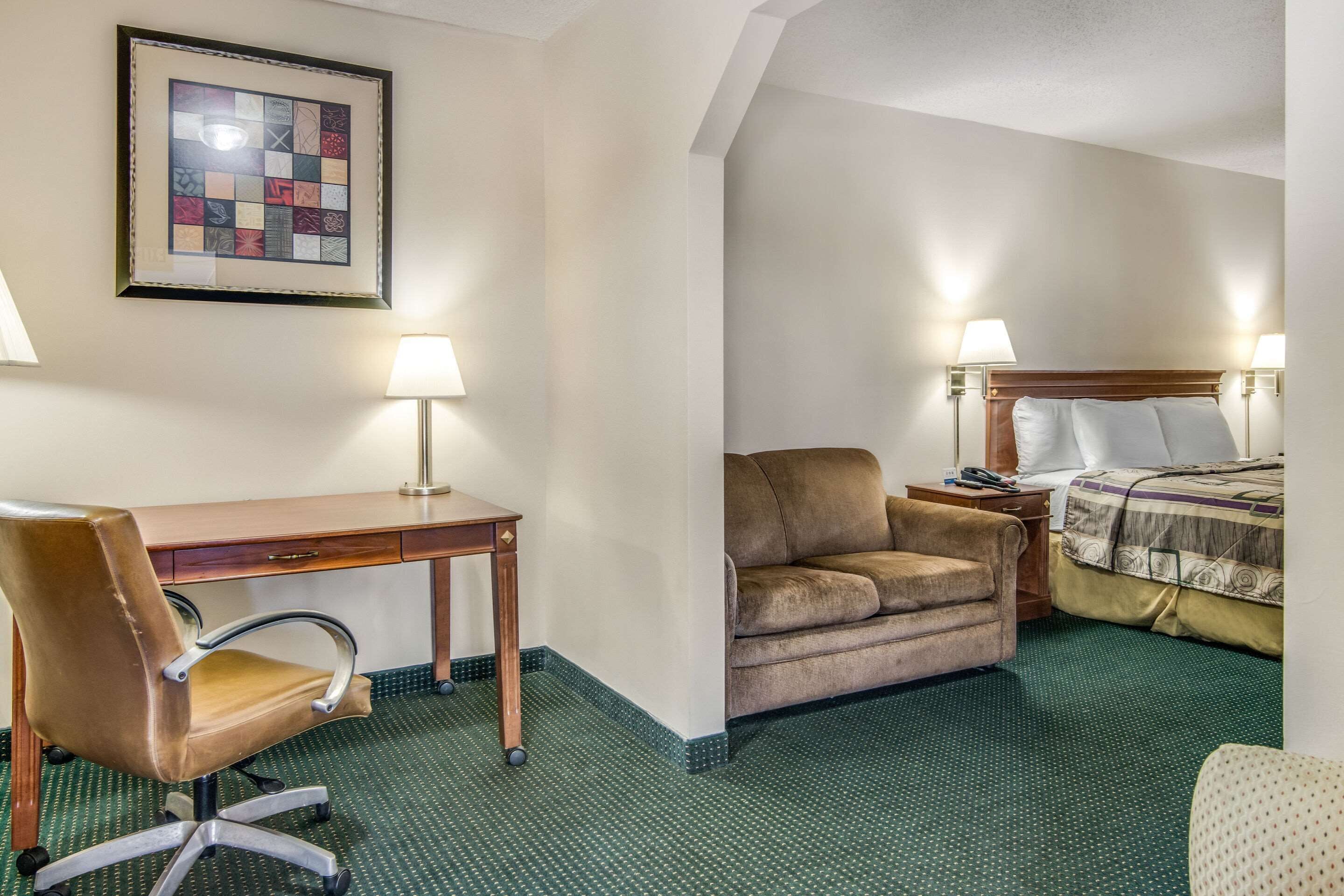 A hotel room with a desk, chair, sofa, and bed.