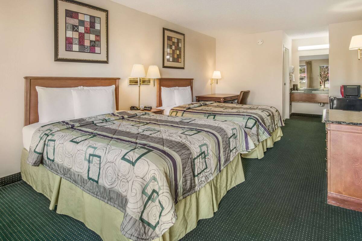 Quarto de hotel com duas camas, uma escrivaninha, um aparador e duas luminárias fixadas na parede.
