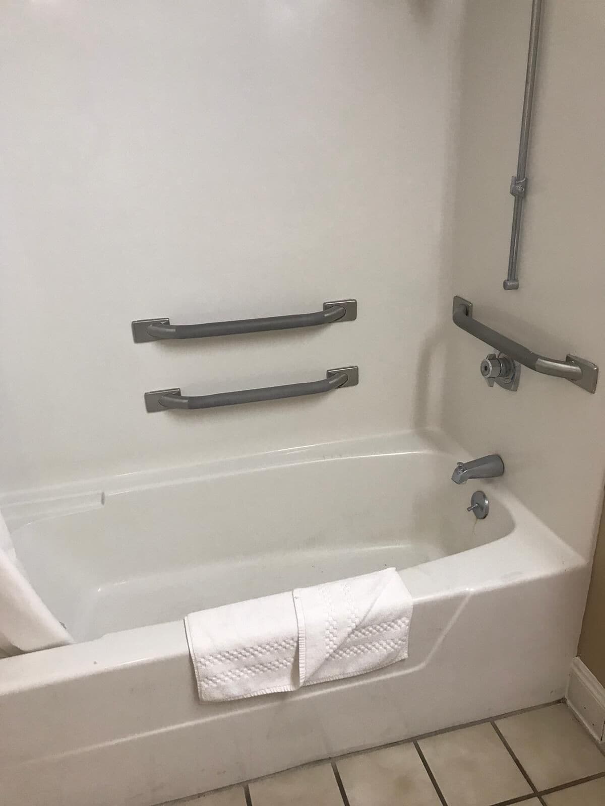 A white bathtub with two grab bars, a towel, and a pipe on the wall.
