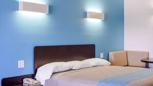 A hotel room with a bed, bedside table, and a small table with a chair. - Motel 6 Canton, TX (Canton)