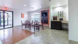 A hotel lobby with a reception desk, a dining area with chairs, a kitchen area, and an exit sign. - Motel 6 Canton, TX (Canton)
