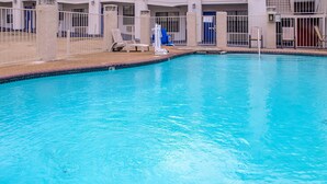 A swimming pool with a tiled edge, surrounded by a white fence and a building with multiple doors and windows. - Motel 6 Canton, TX (Canton)