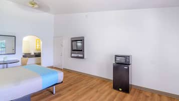 A hotel room with a bed, a microwave, a TV, and a small kitchenette area.