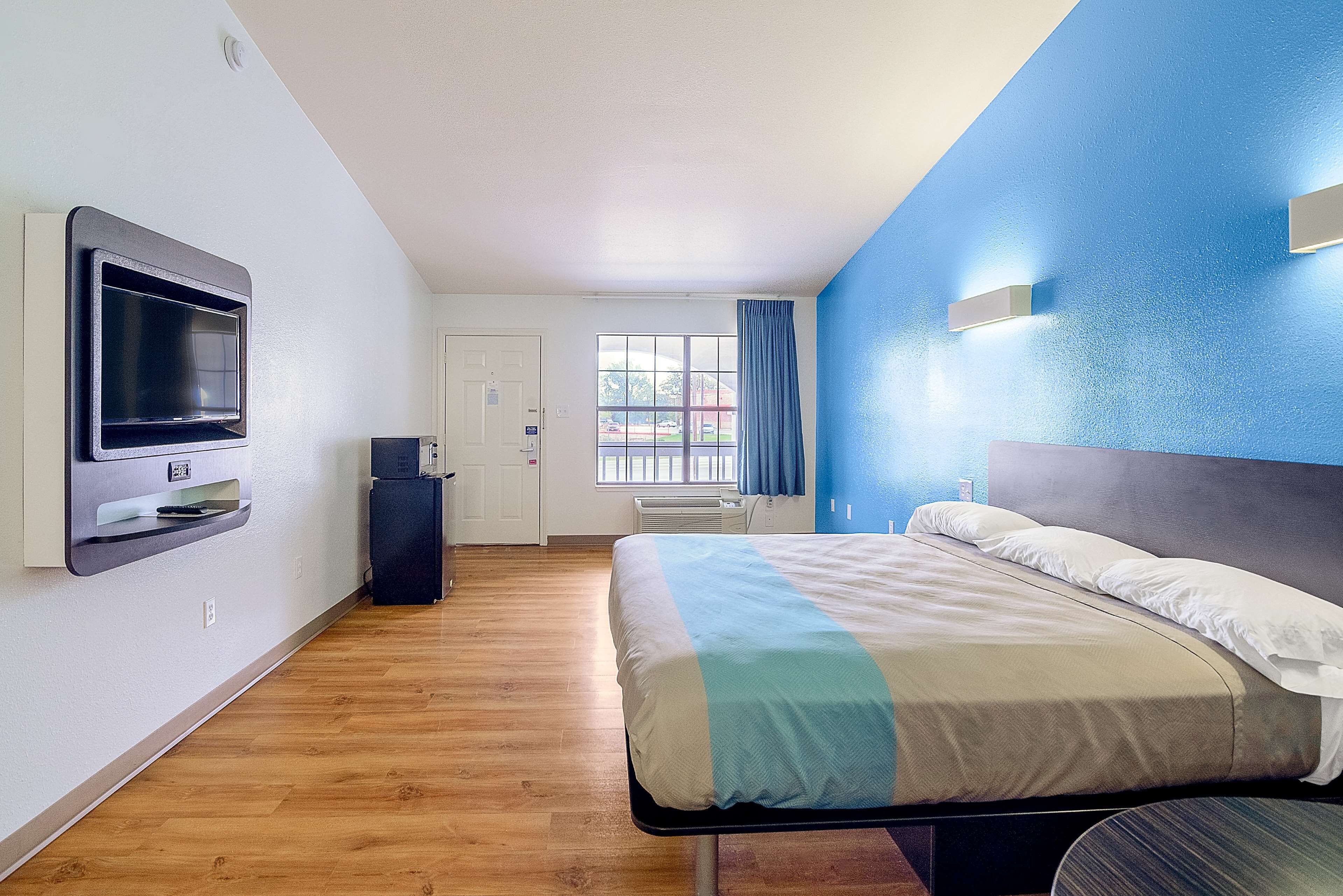 Une chambre d’hôtel avec un lit, un téléviseur fixé au mur, une fenêtre avec des rideaux et une porte.