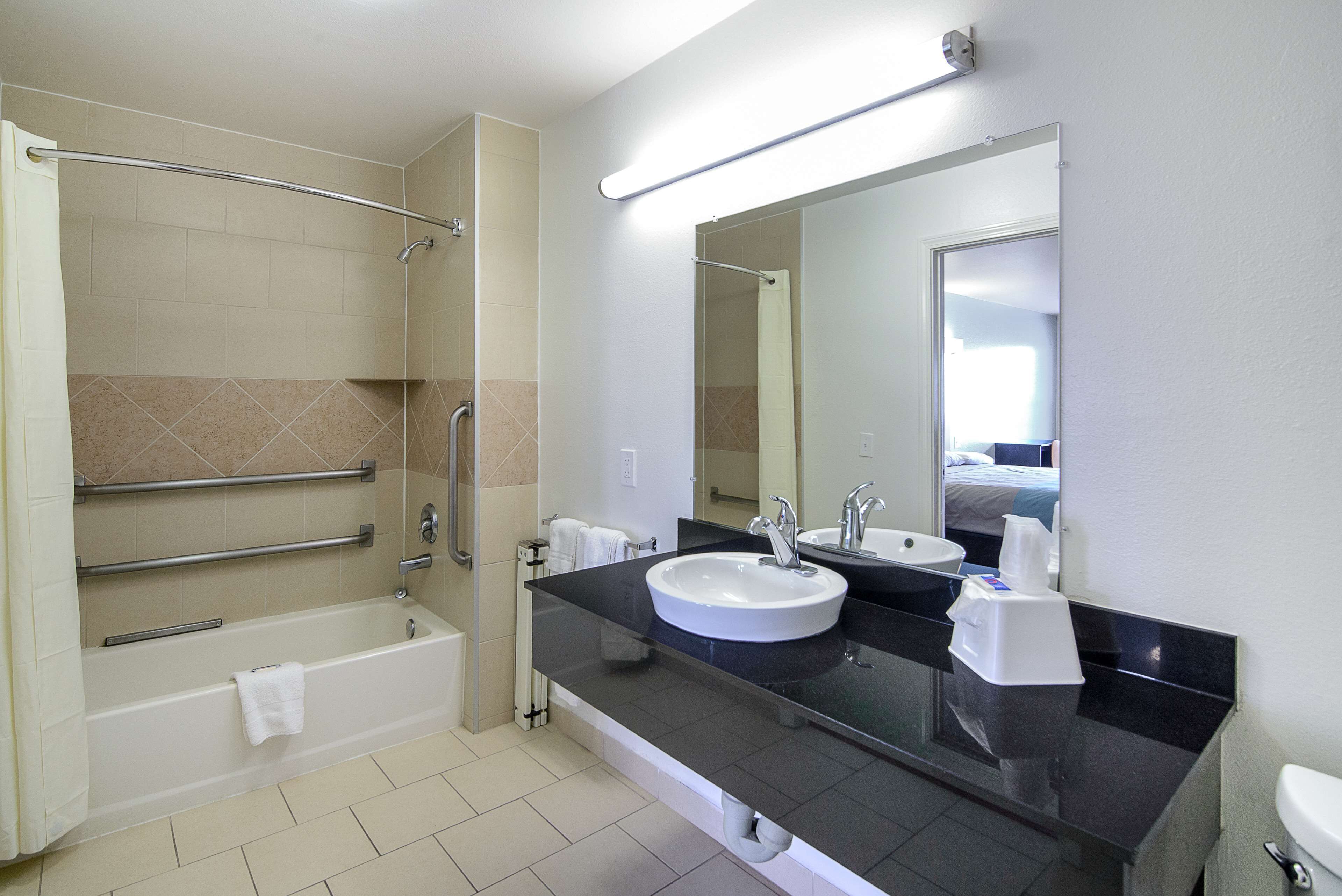 A modern bathroom with a bathtub, a large mirror, a sink, and a toilet.