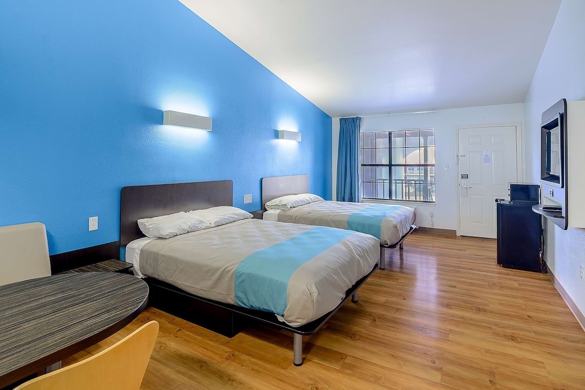 Habitación de hotel con dos camas, un escritorio y un televisor.